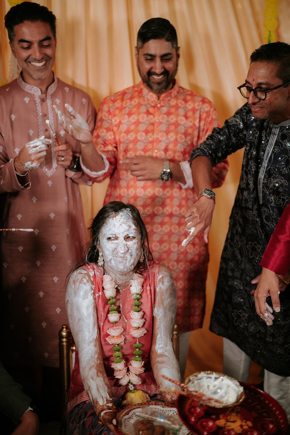Groom covered in white paste during Indian Haldi ceremony, surrounded by smiling men in traditional kurtas.