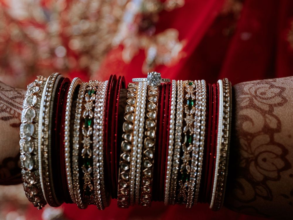 Close-up of a bride's wrist adorned with traditional red and gold Indian bangles with intricate henna designs.
