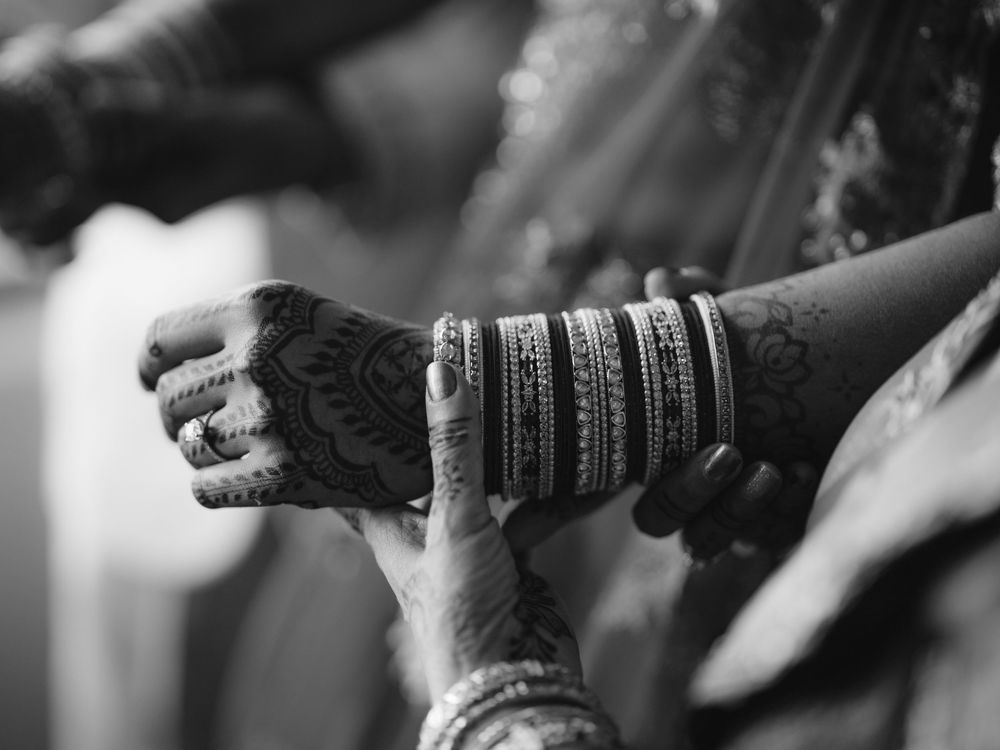 Close-up black and white photo of henna-adorned hands with bangles during Indian bridal preparation.