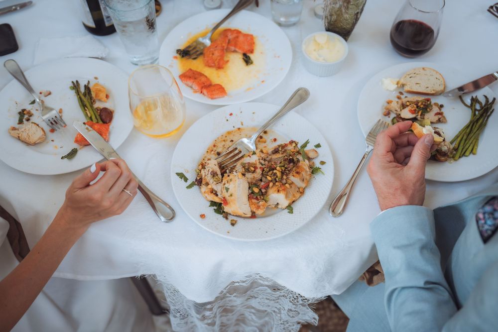 Two people dining at an elegant table with gourmet dishes, wine glasses, and white linen tablecloth at a fine restaurant.