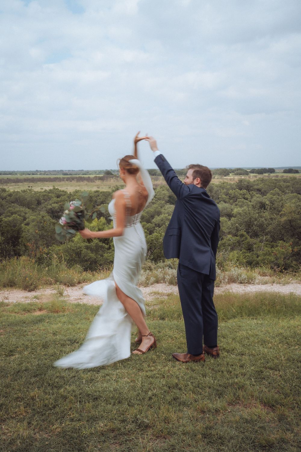 Bride and groom dancing outdoors on their wedding day with scenic green landscape in the background.
