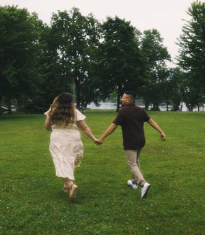 Couple holding hands and running through a green park toward a lake.