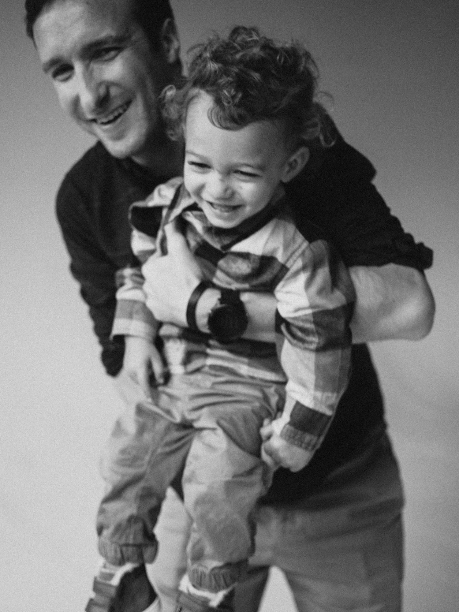Black and white photo of a smiling man holding a laughing toddler boy in a plaid shirt.
