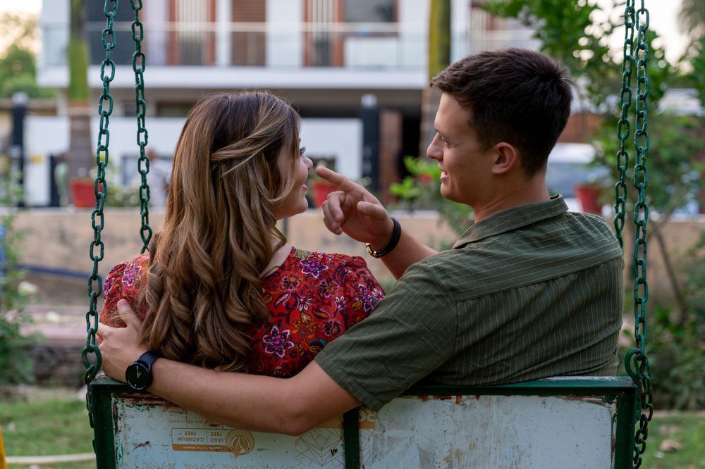 Close-up candid shot of a man with his arm around a woman, softly touching her face while sitting outdoors together.