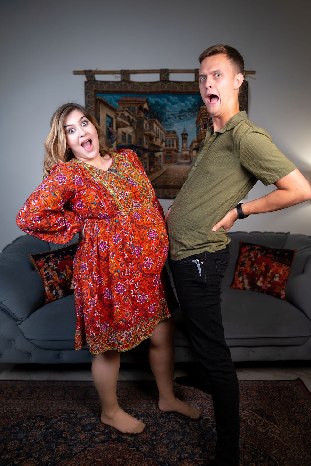 Candid and humorous indoor photography of a cheerful man and woman posing together with playful expressions in a living room studio setting.