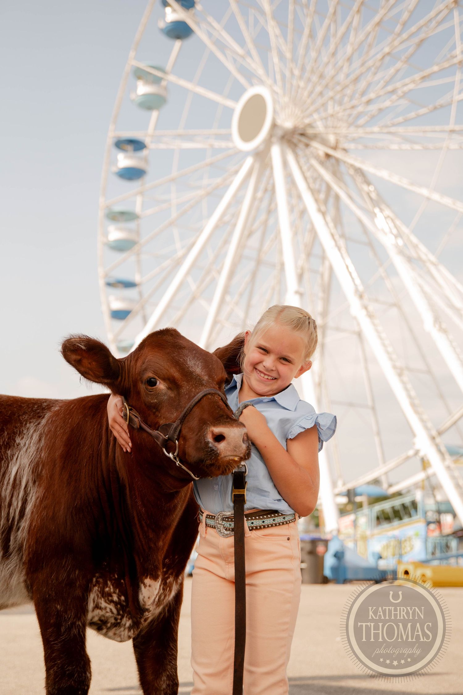 Young girl smiles hugging a brown cow at a county fair with a Ferris wheel in the background.