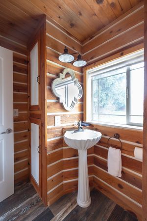 Rustic log cabin bathroom with pedestal sink, art deco mirror, and wood plank walls.