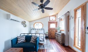 Bright tiny home interior with wood ceiling, ceiling fan, blue sofa, and barn door.