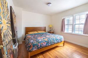 Bedroom with wood-framed bed, colorful quilt, hardwood floors, and large decorative wall tapestry.