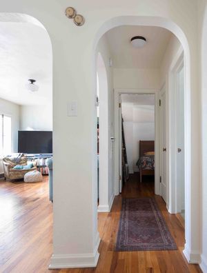 Bright hallway with elegant arched doorways, hardwood floors, runner rug, and view into living room.