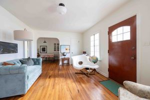 Cozy living room with hardwood floors, blue sofa, arched doorway, and warm wood front door.