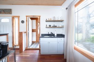 White kitchen with dark countertop, open shelving, hardwood floors, and natural light from large window.