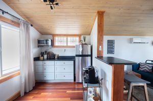 Compact kitchen with wood ceiling, stainless appliances, cherry hardwood floors, and mini-split AC unit.