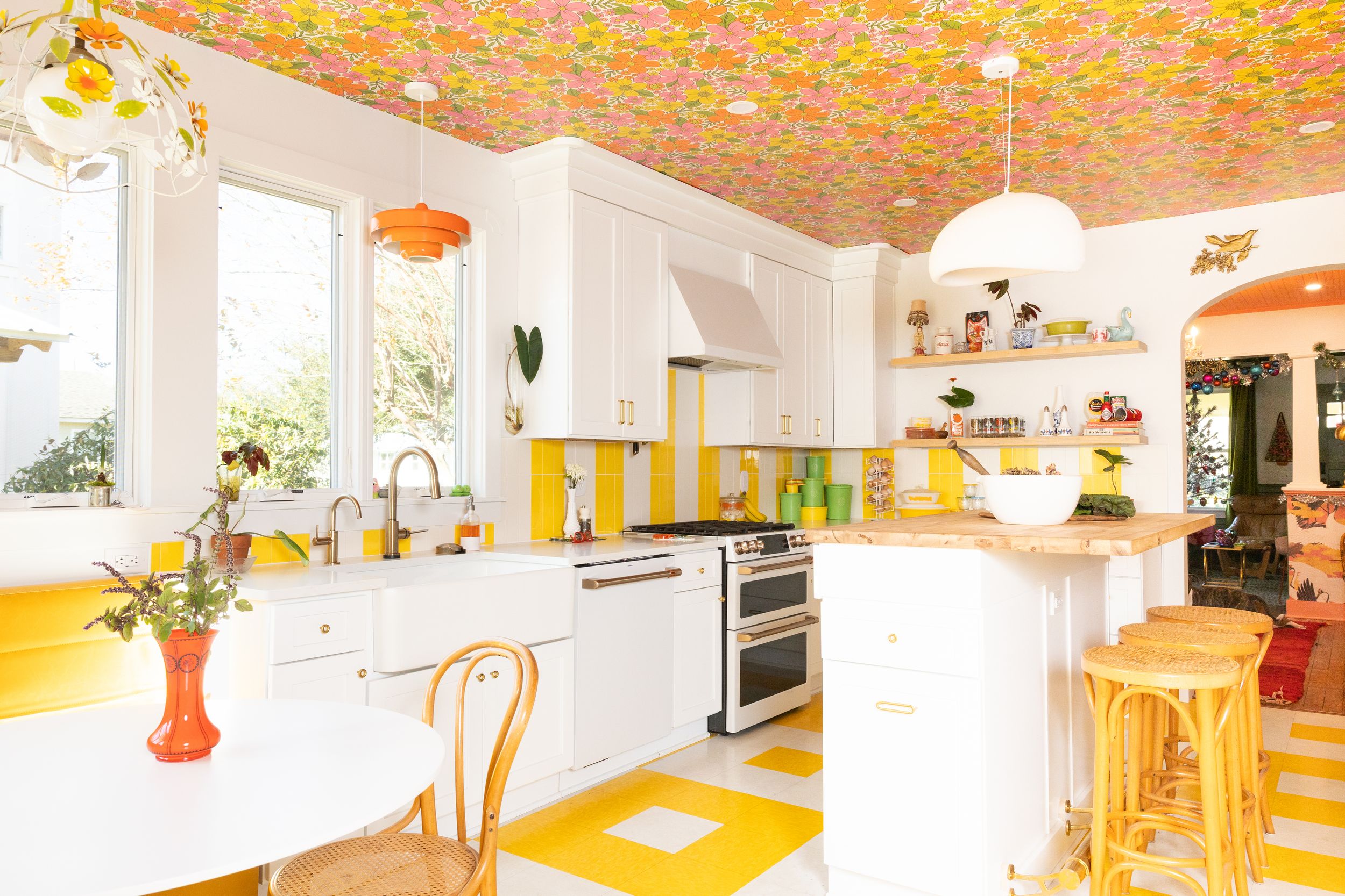 White kitchen with bold floral ceiling, yellow accents, checkerboard floors, and island seating.