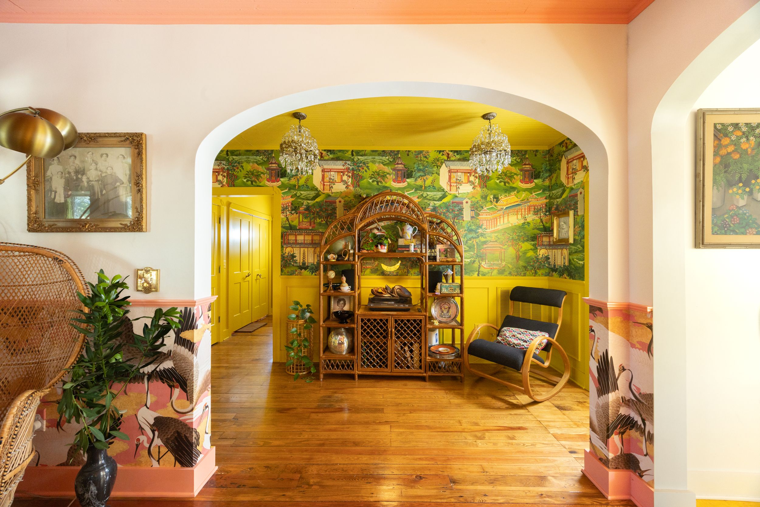 Colorful home interior with arched doorways, yellow walls, tropical mural, and rocking chair.