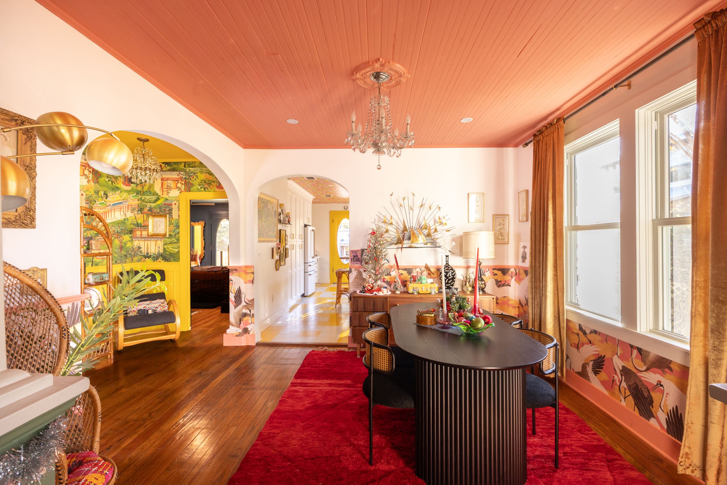 Dining room with coral painted ceiling, red rug, arched doorway, and tropical mural beyond.