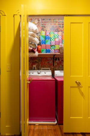 Colorful laundry room with pink washer and dryer behind bright yellow doors.