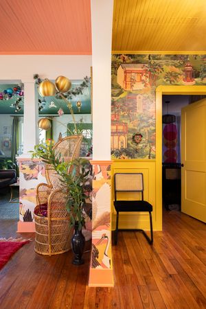 Vibrant eclectic hallway with chinoiserie wallpaper, yellow ceiling, and wicker peacock chair.