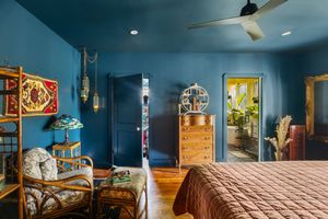 Moody blue bedroom with rattan furniture, brass accents, and warm wood floors.