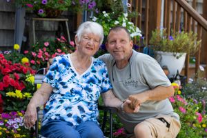 Elderly couple smiling together in a vibrant garden filled with colorful summer flowers in bloom.
