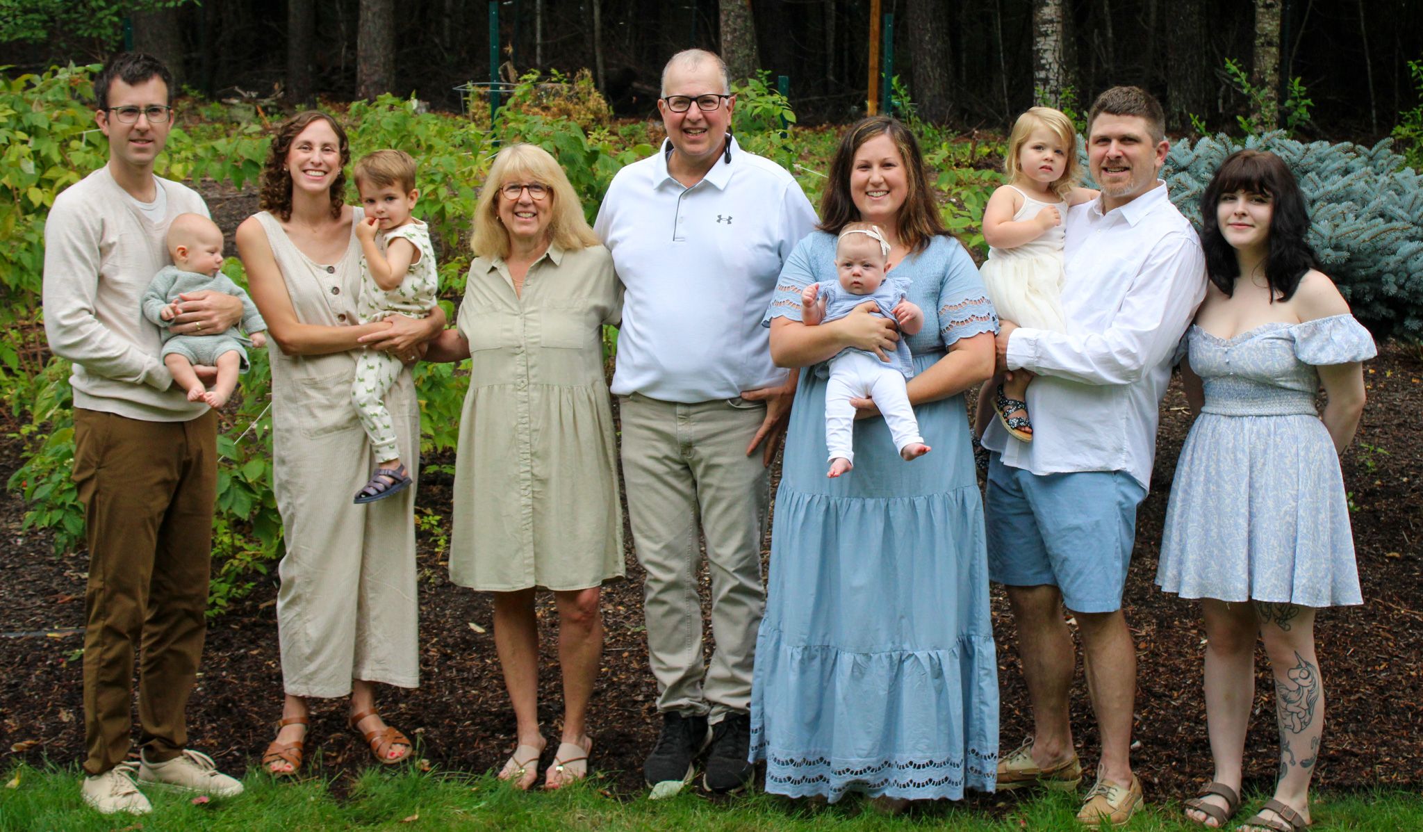 Large multigenerational family group portrait outdoors in lush green garden setting.
