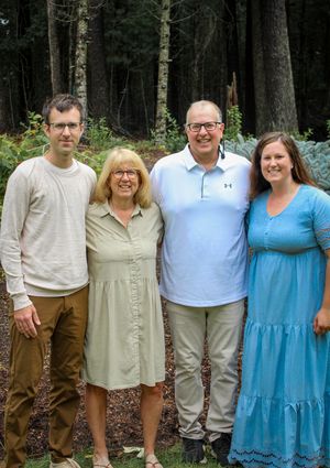 Four smiling adults pose together in wooded forest garden outdoor setting.