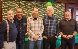 Five men smiling together at an indoor celebration with green balloon decorations.
