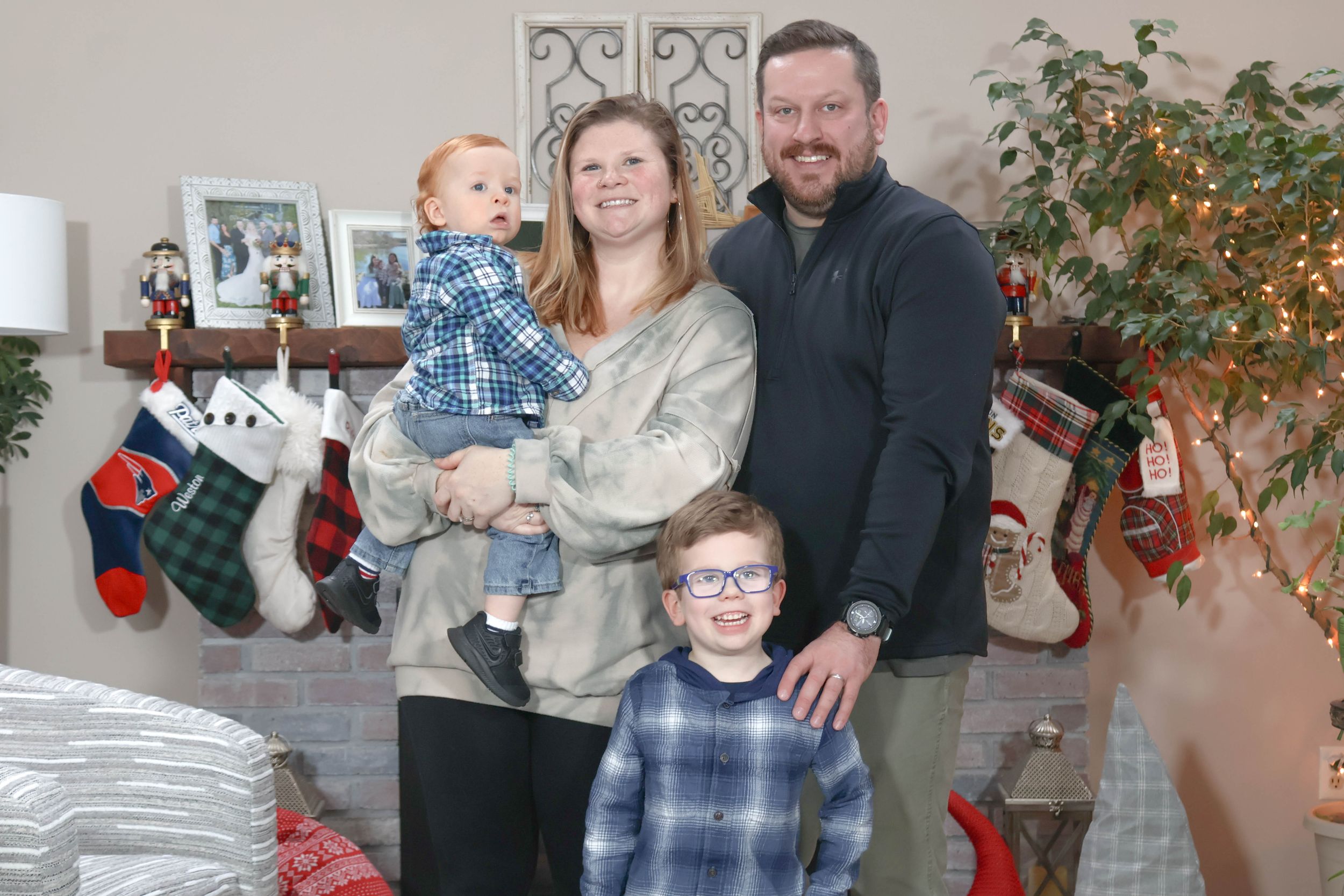 Family of four poses near a fireplace with Christmas stockings and holiday decorations.