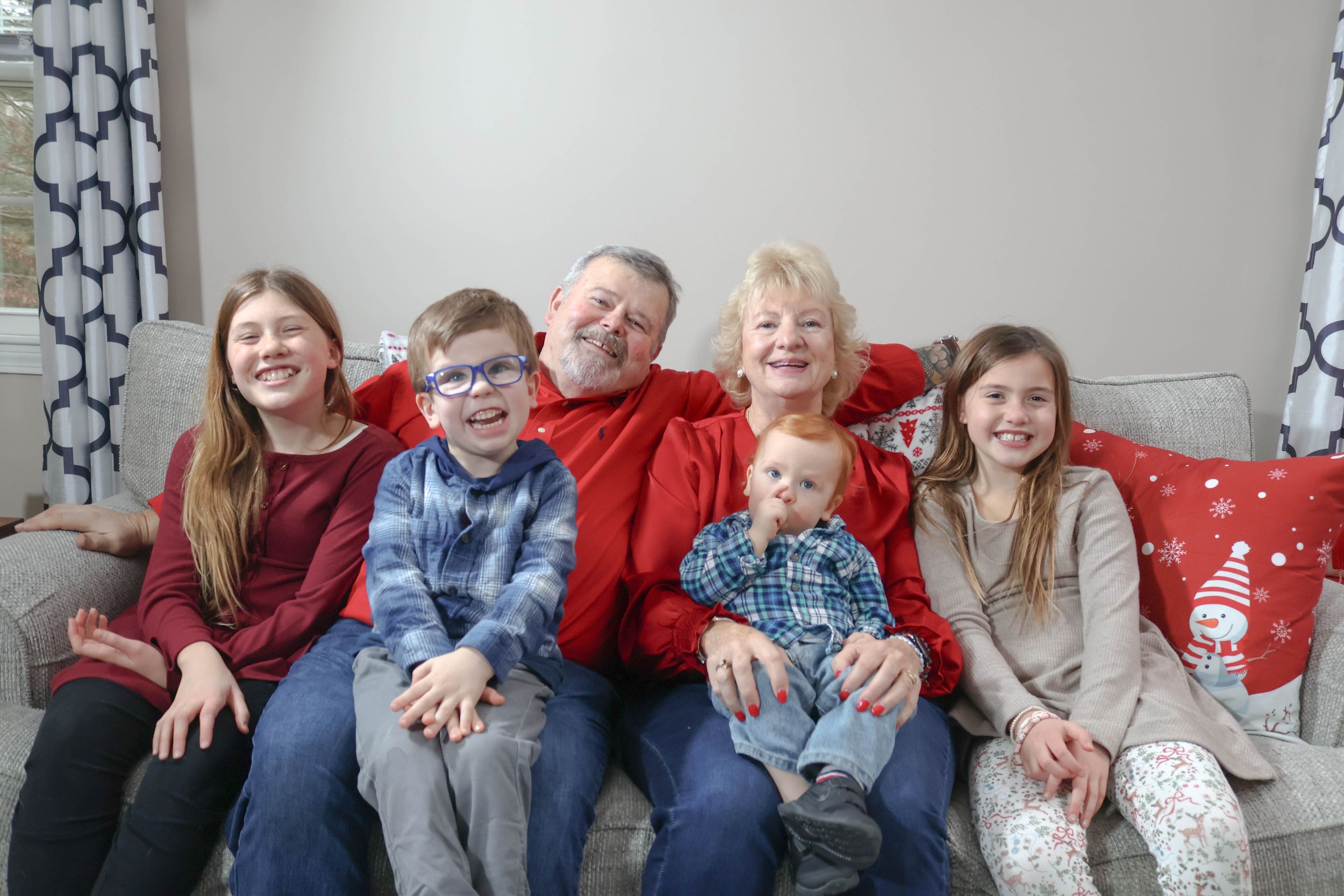 Grandparents sitting on a sofa with four grandchildren during a holiday family gathering.