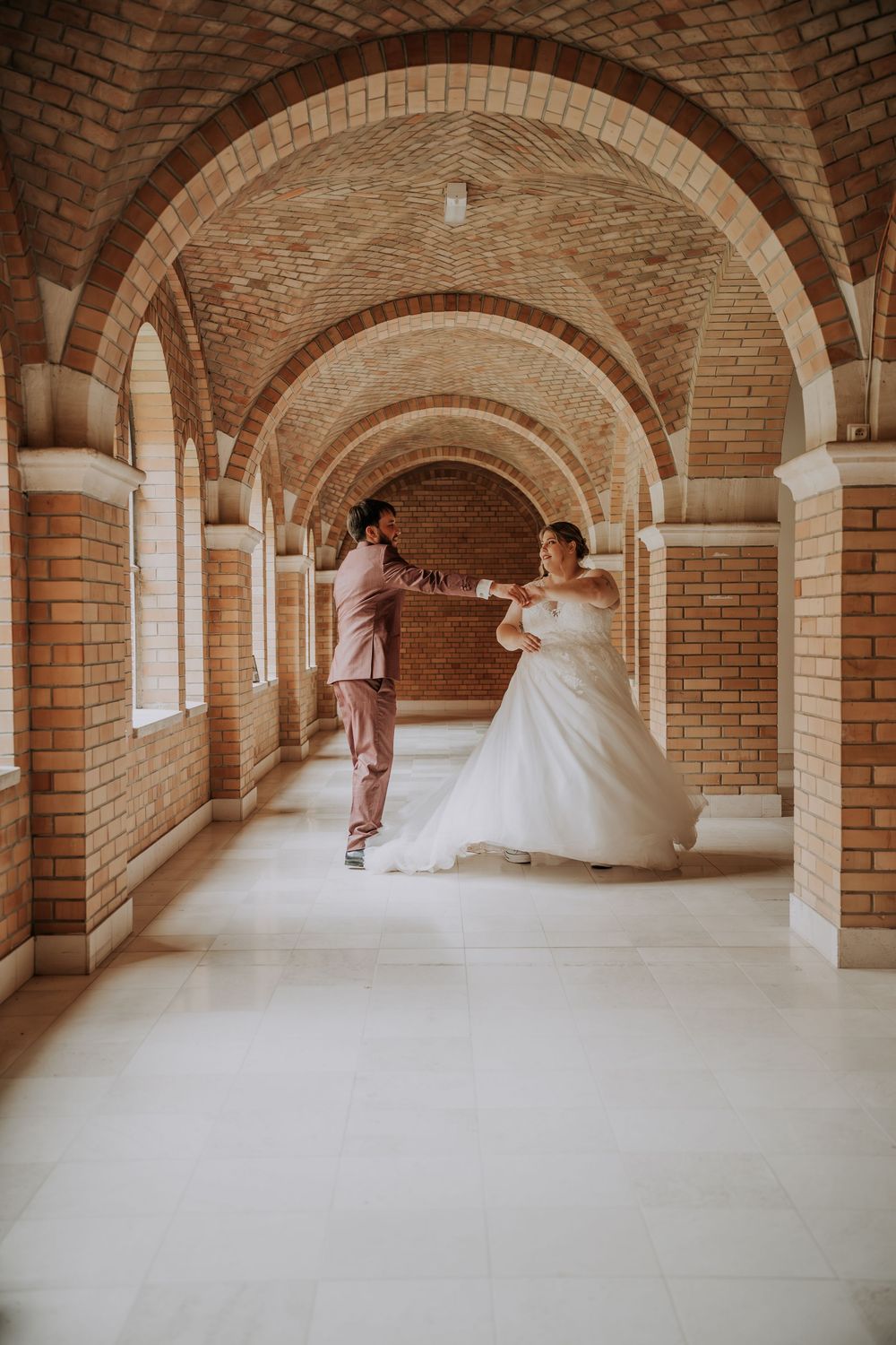 Bride and groom dancing in an elegant brick archway corridor, bride in a flowing white ball gown.