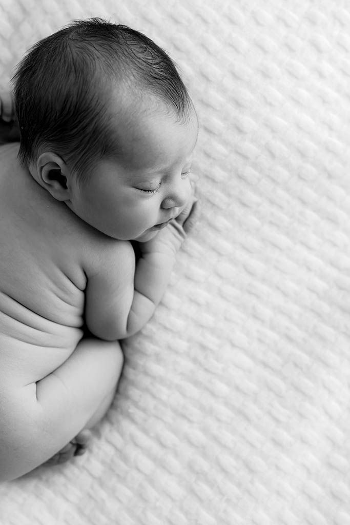 Black and white photo of a sleeping newborn baby lying on a white textured blanket.