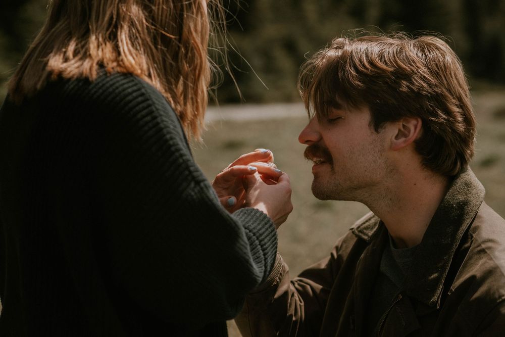 Man on one knee placing a ring on a woman's finger during a romantic outdoor marriage proposal.