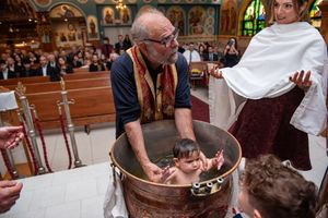 Orthodox priest baptizes a baby by immersion in a large copper baptismal font during a church ceremony.