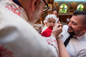 Orthodox priest anoints baby in white bonnet held by father during a traditional christening ceremony.