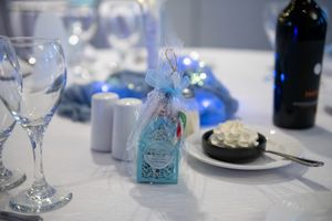 Elegant baptism party table setting with blue decorative gift box, wine glasses, candles, and dessert.