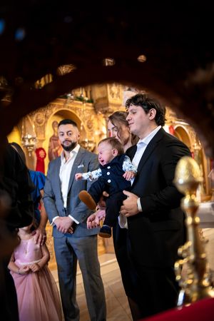 Family members holding a baby in a beautifully decorated Orthodox church during a baptism.