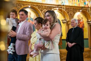 Family poses with infant during Orthodox christening ceremony in ornate golden church interior.