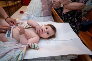 Baby lying on changing table during Orthodox baptism preparation ceremony in church.