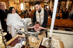 Crying baby being baptized in ornate font during Orthodox Christian church ceremony.