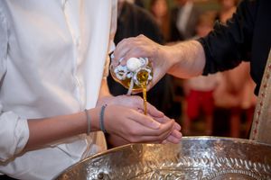 Priest pouring holy oil over hands during an Orthodox Christian baptism ceremony.