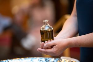 Hands holding a glass bottle of holy anointing oil during an Orthodox baptism ceremony.