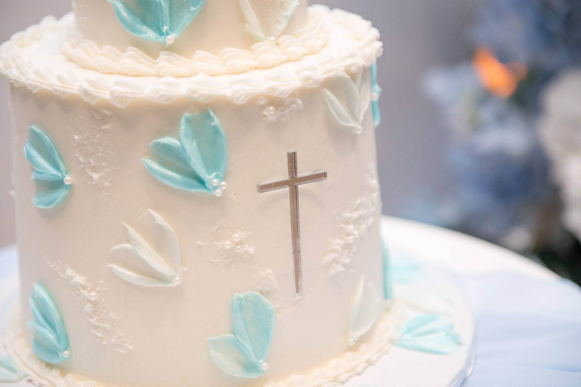 A white two-tier baptism cake decorated with blue butterflies and a silver cross.