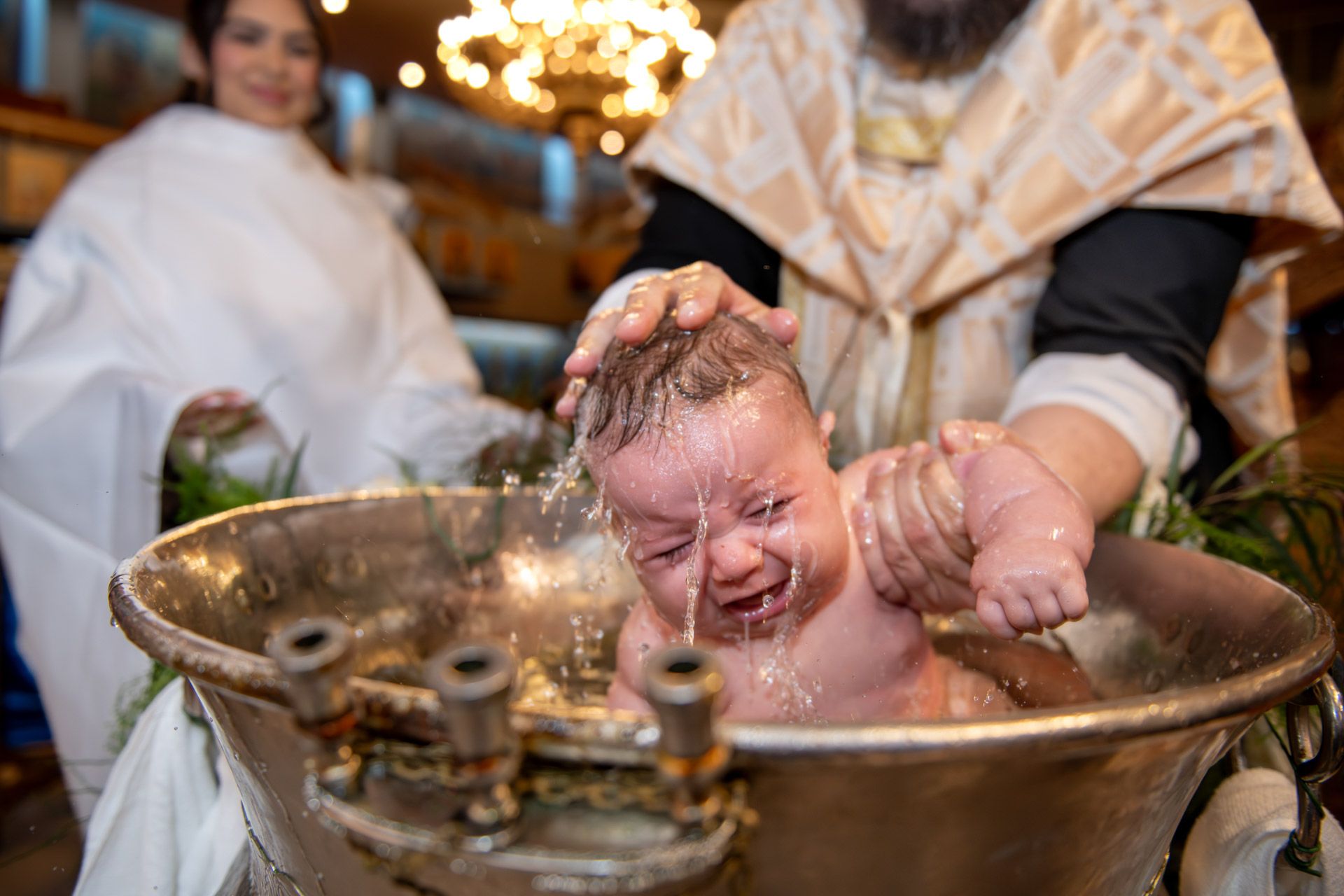A baby cries as a priest pours water over its head during an Orthodox baptism ceremony.