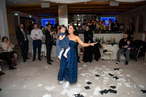 A woman in a blue gown dances with a toddler amid falling confetti at a baptism party.
