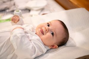 A peaceful baby in white clothing lies on a soft surface, smiling gently.