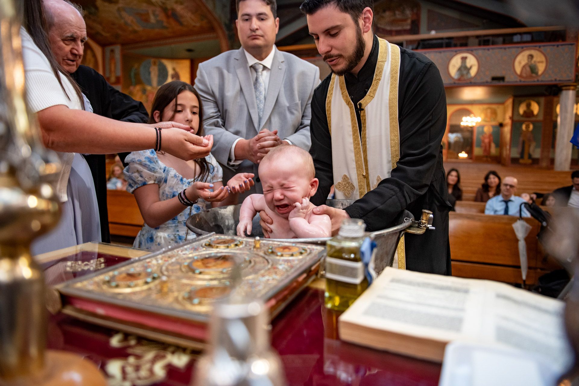 Crying baby lifted from baptismal font by Orthodox priest during christening ceremony.