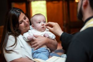 Orthodox priest anointing baby with chrism oil during baptism ceremony in church.
