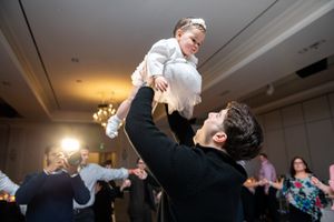 A man joyfully lifts a baby dressed in white at a celebratory baptism reception.