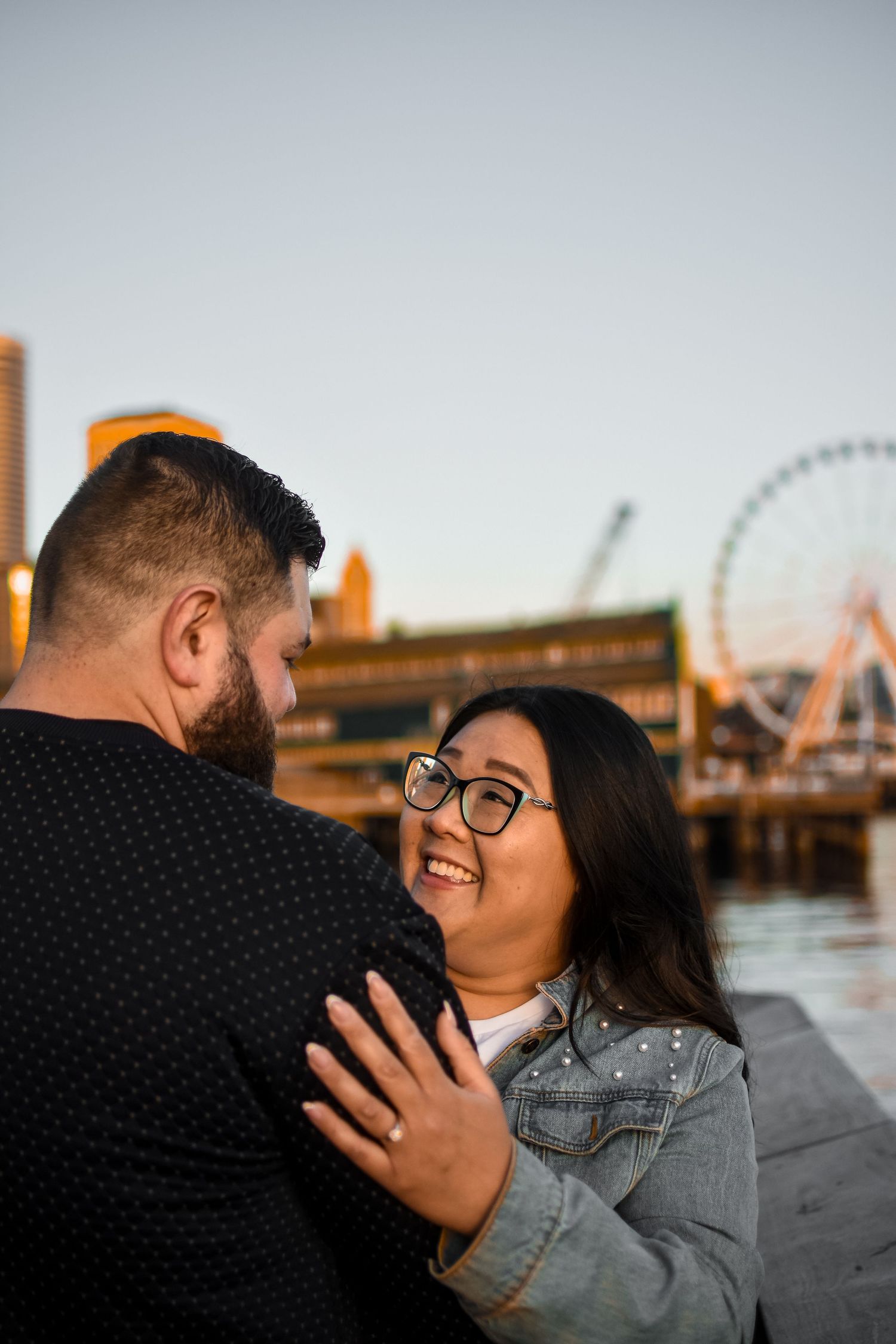 A couple shares a romantic moment at sunset near the Seattle waterfront with the Great Wheel visible in the background.