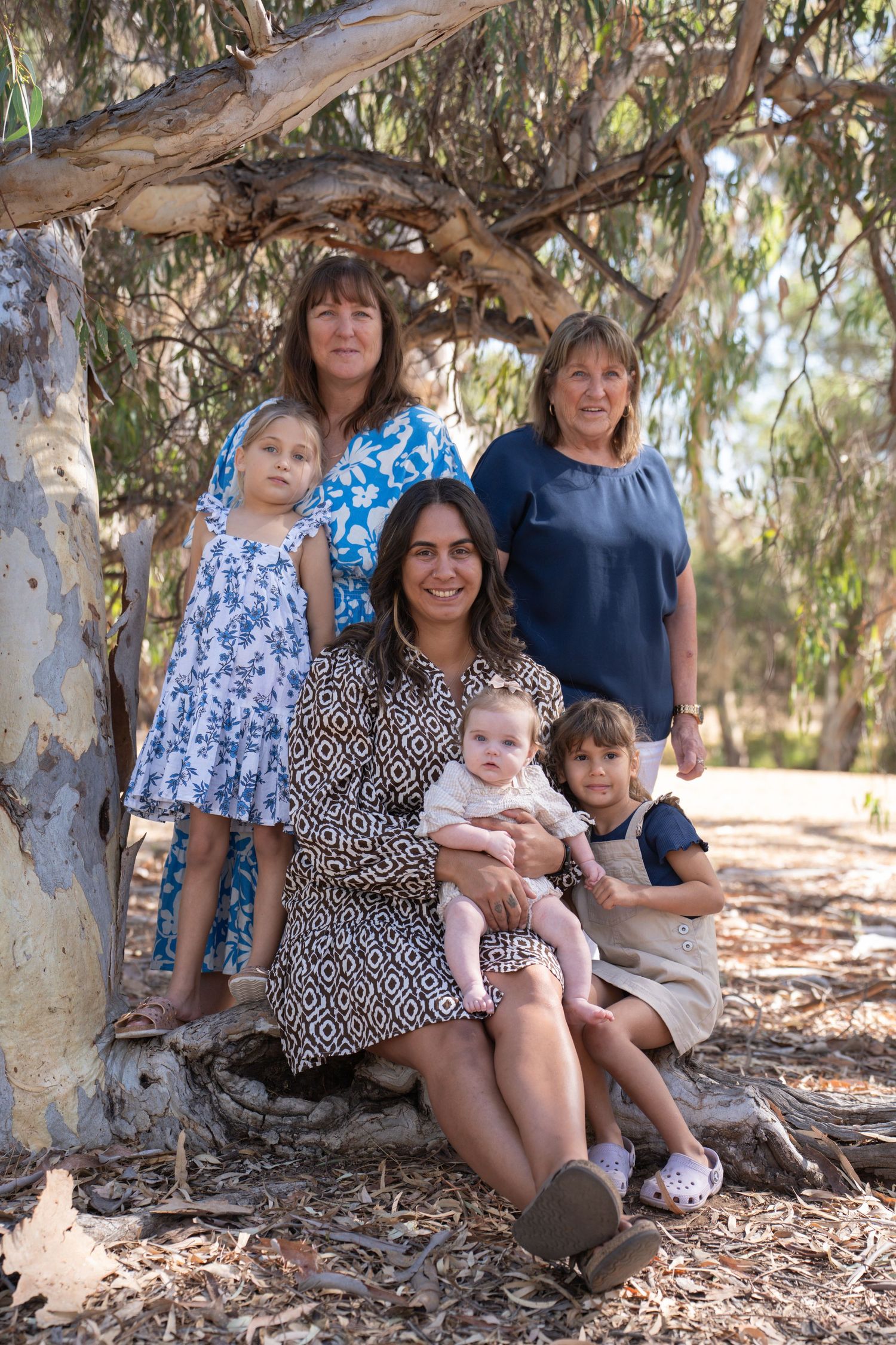 A family group poses together under a eucalyptus tree on a sunny day in nature.